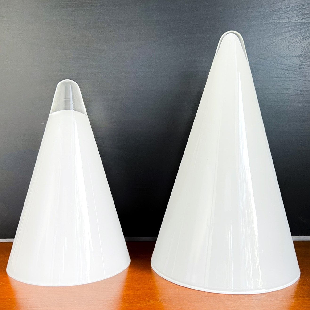 Two white cone-shaped lamps on a wooden surface with a dark background