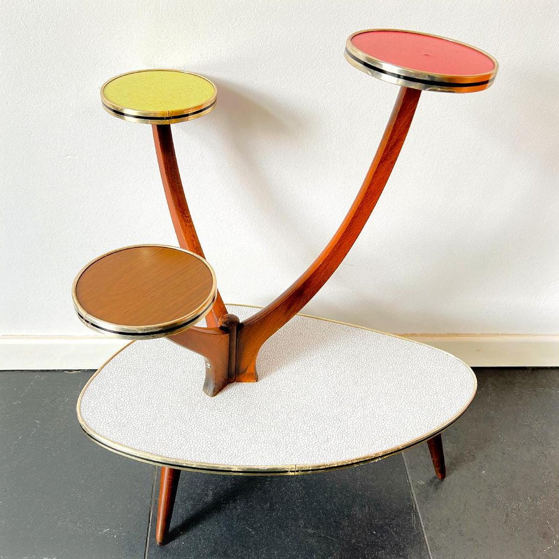 Mid-Century Modern plant stand with three colorful formica shelves on wooden base.