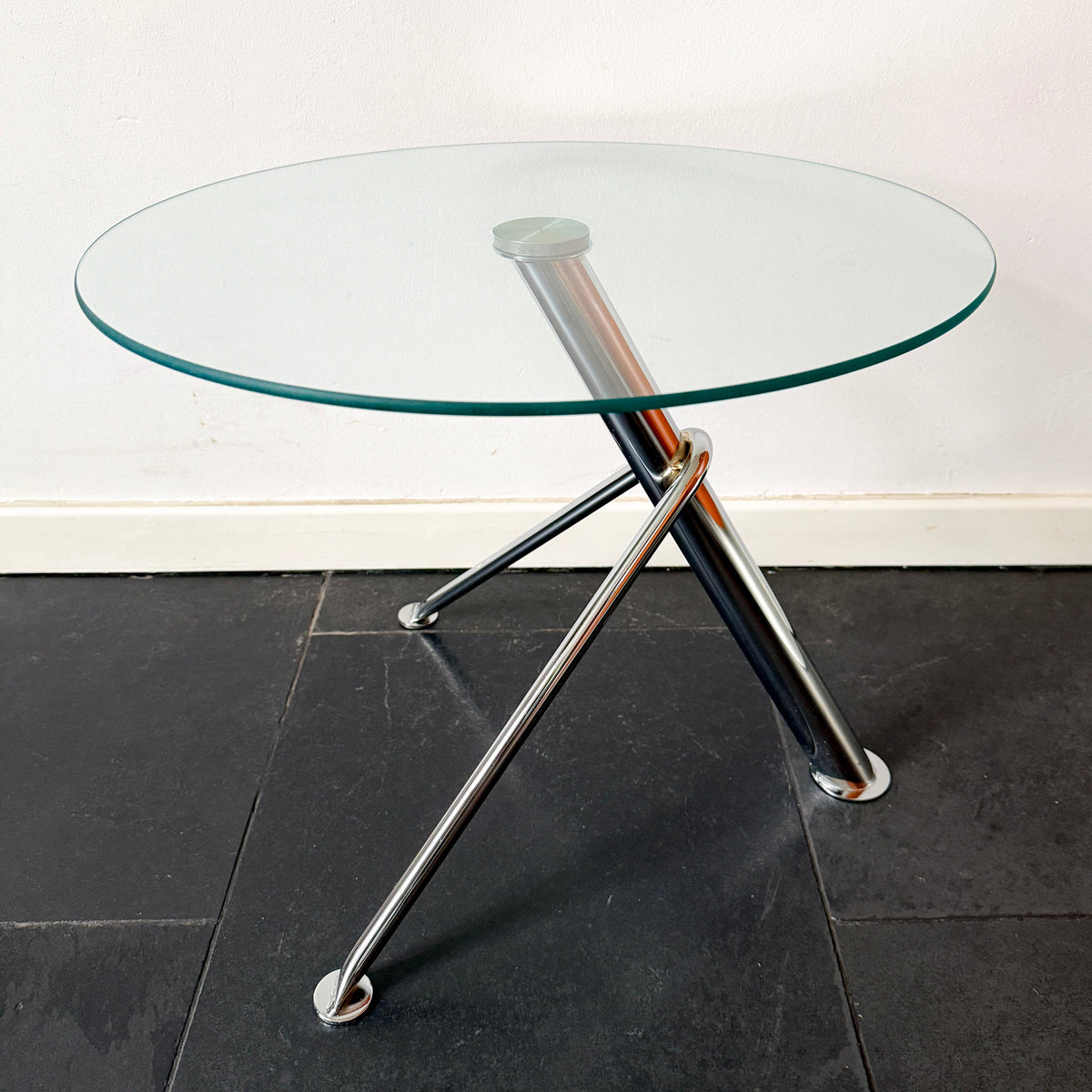 Modern minimalist round side table with clear glass tabletop and sculptural chrome-finished metal tripod base.