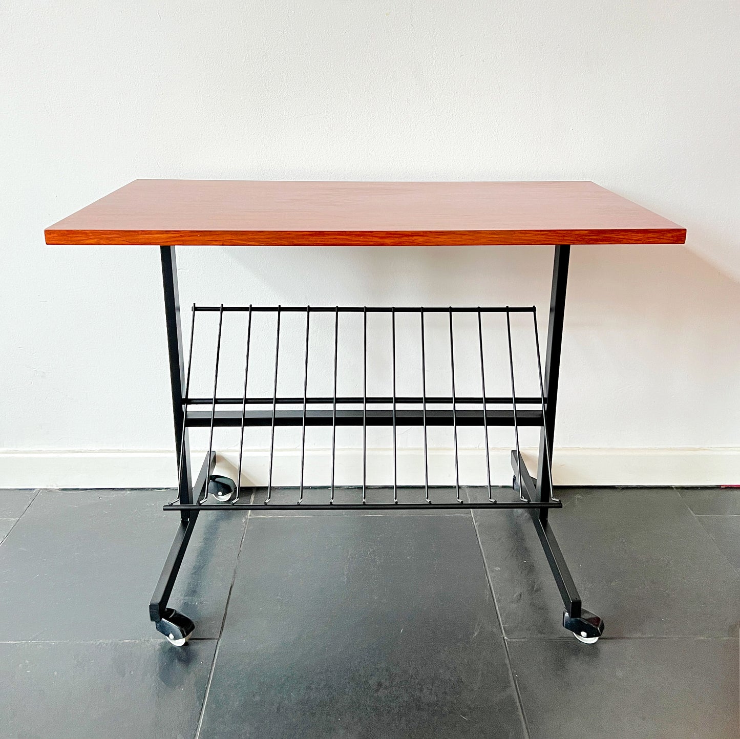 Mid-Century Modern wheeled table with wooden top and black metal frame, magazine rack beneath, vintage.