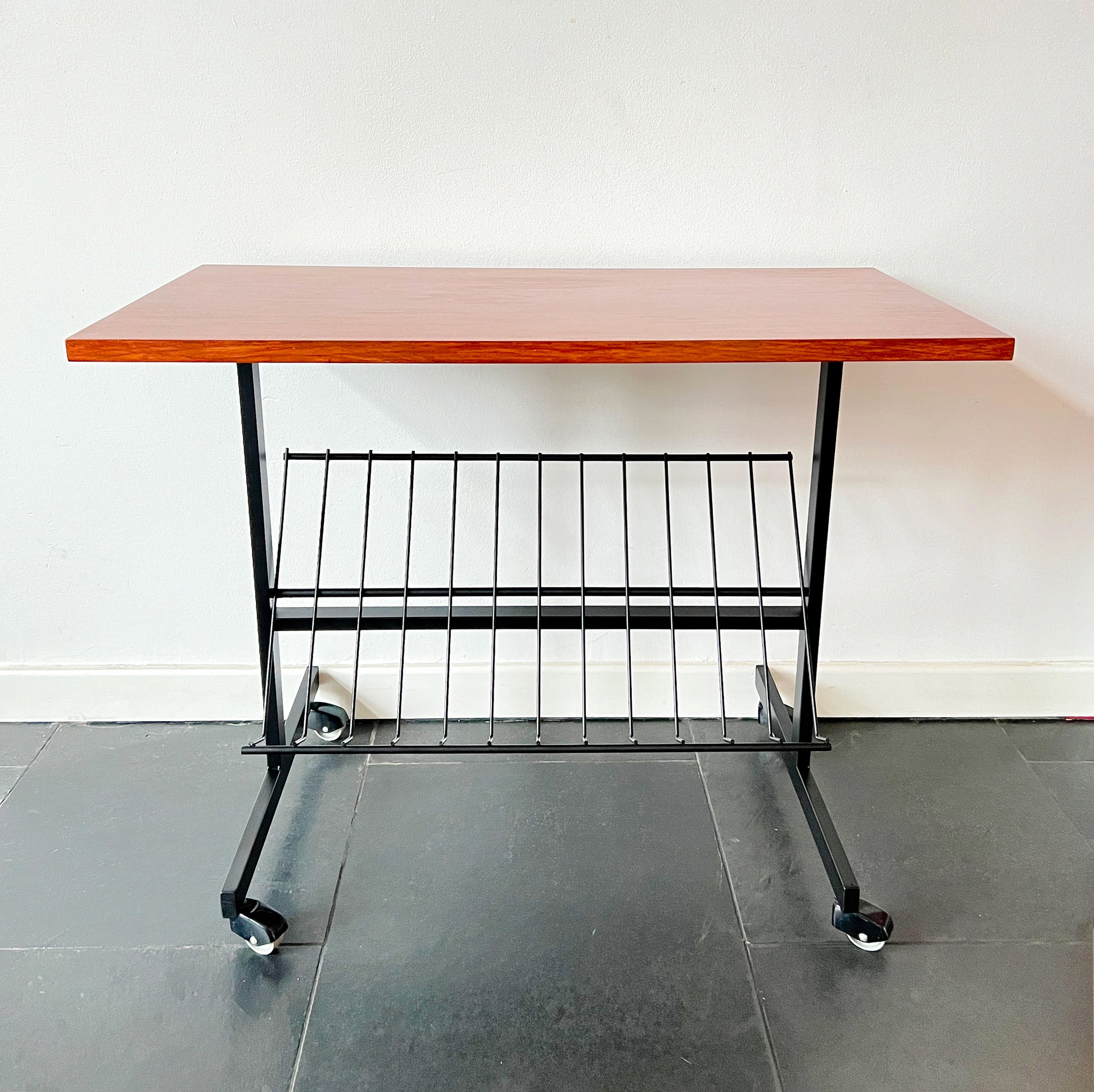 Mid-Century Modern wheeled table with wooden top and black metal frame, magazine rack beneath, vintage.